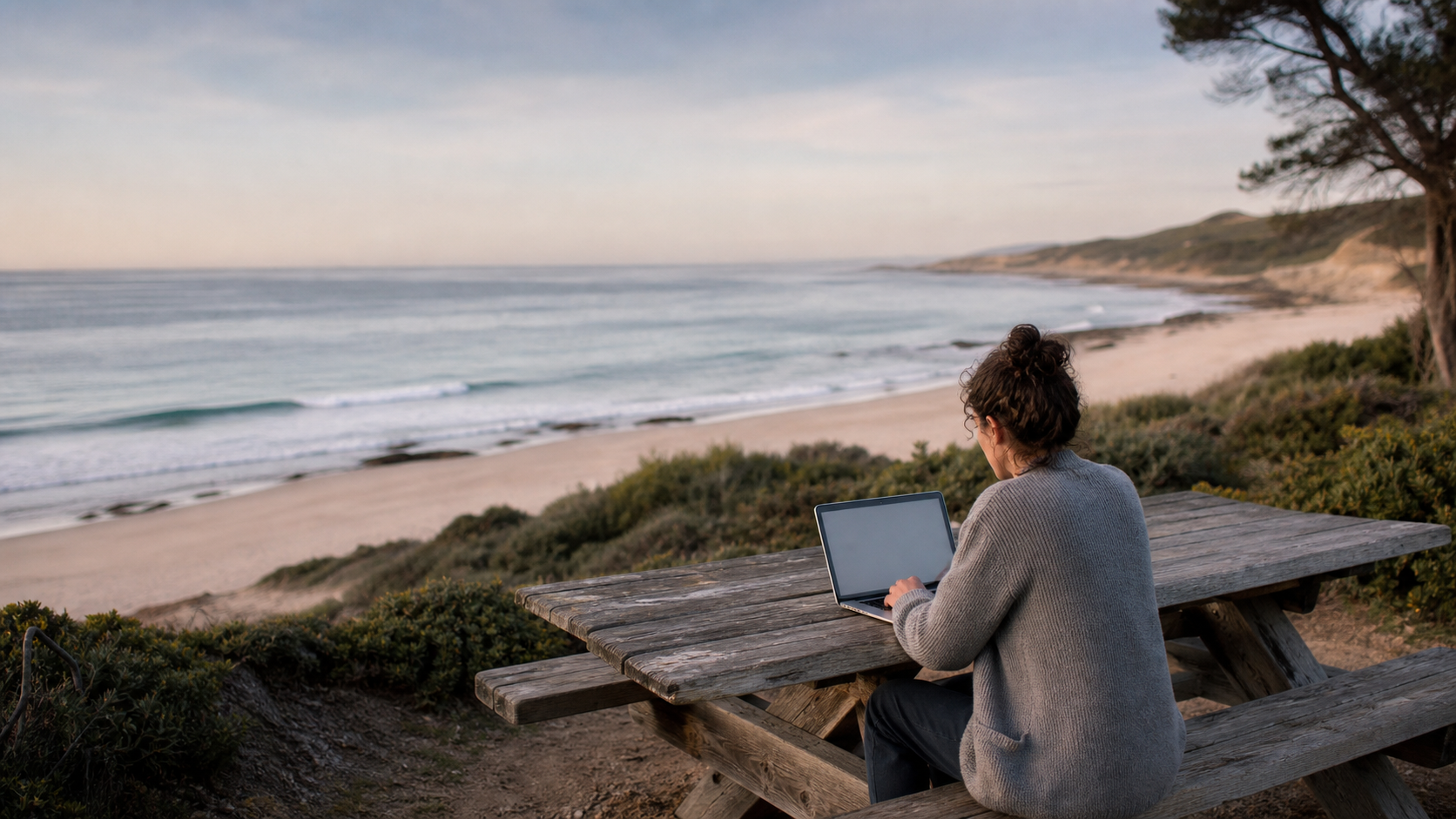 A solo founder working from a picnic table overlooking the beach